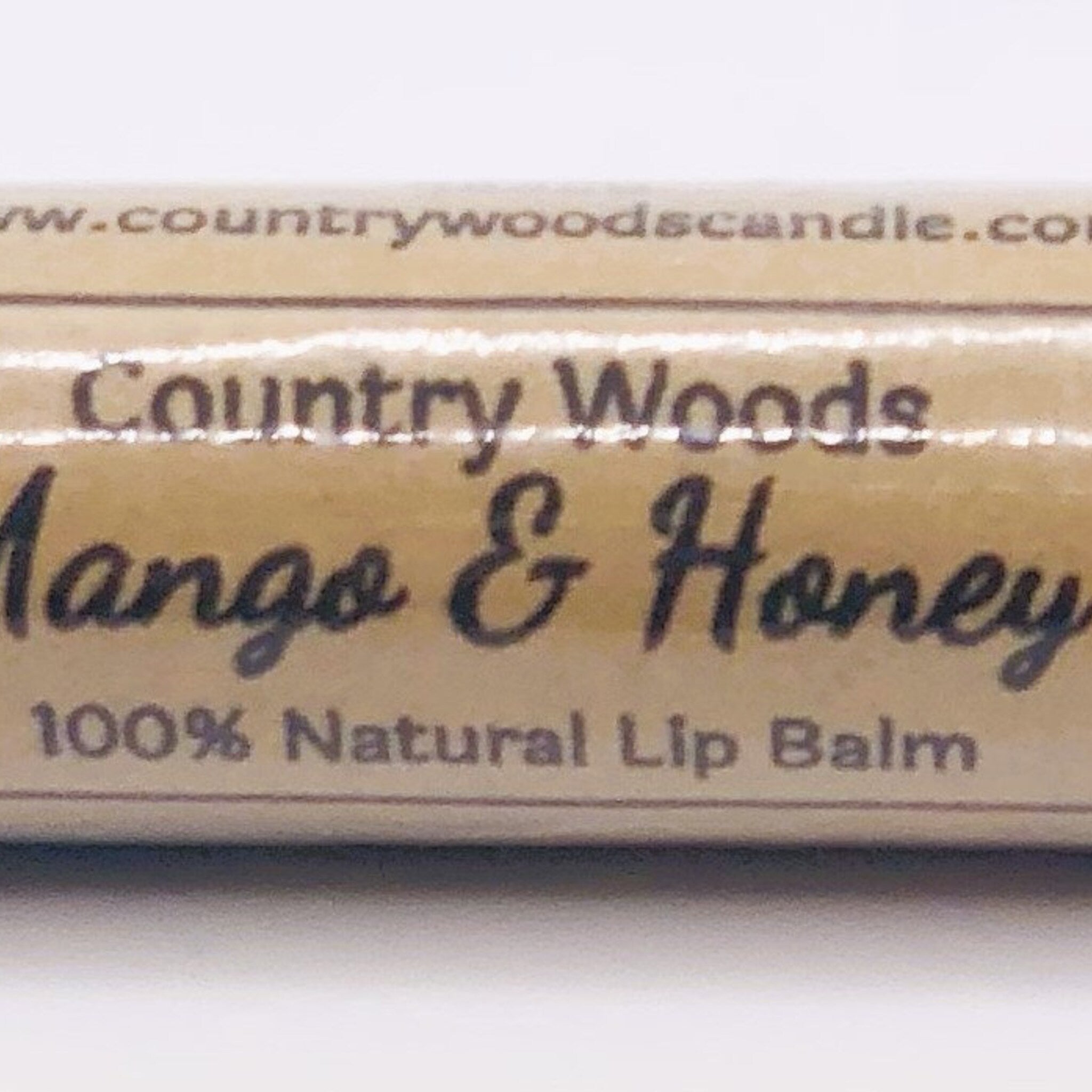 Lip balm with "Mango & Honey" text, tan and black lettering, and "Country Woods" brand name.