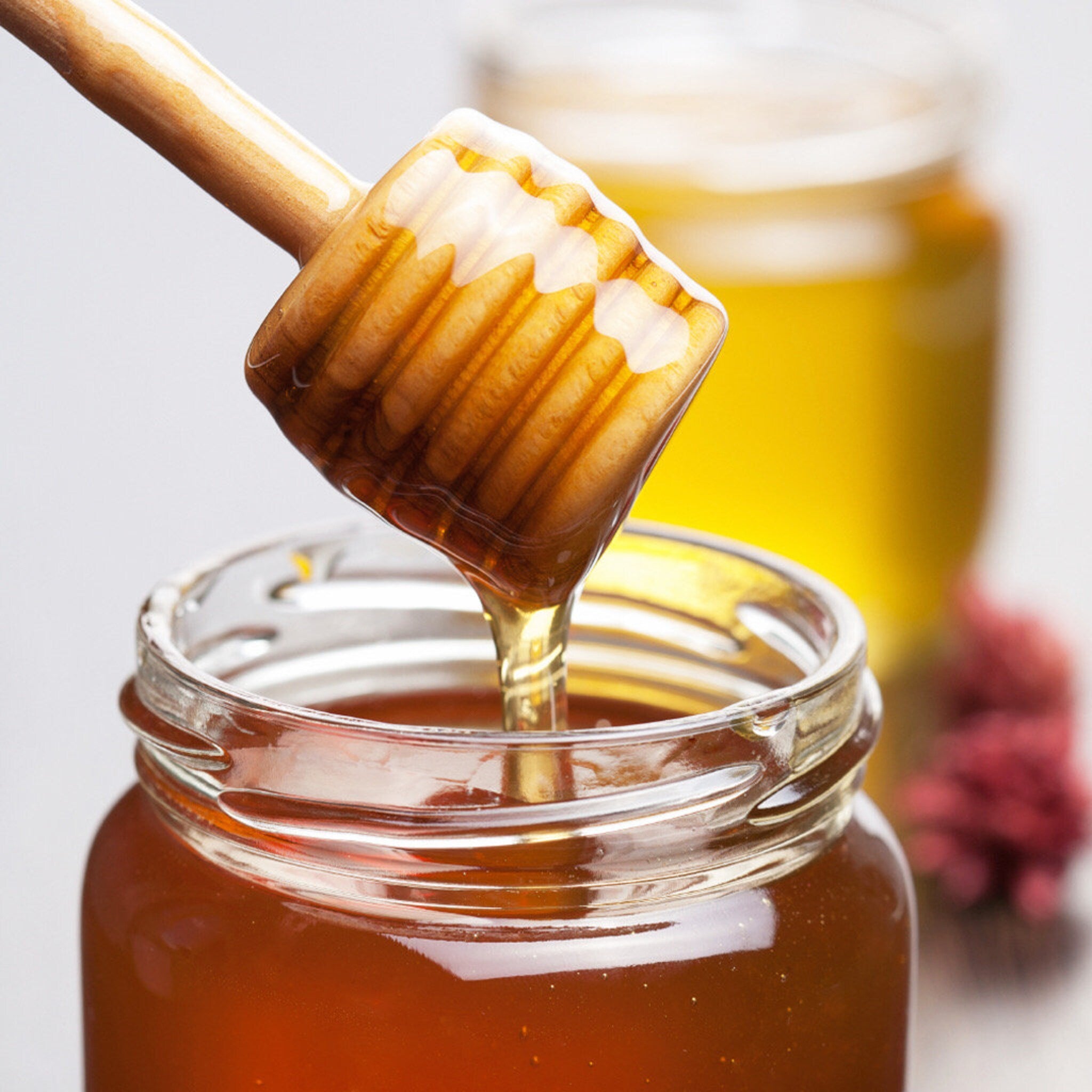 Honey dipper with dripping honey, wooden handle, glass jar, amber liquid