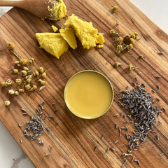 Yellow balm in gold tin, with dried chamomile and lavender on wood surface
