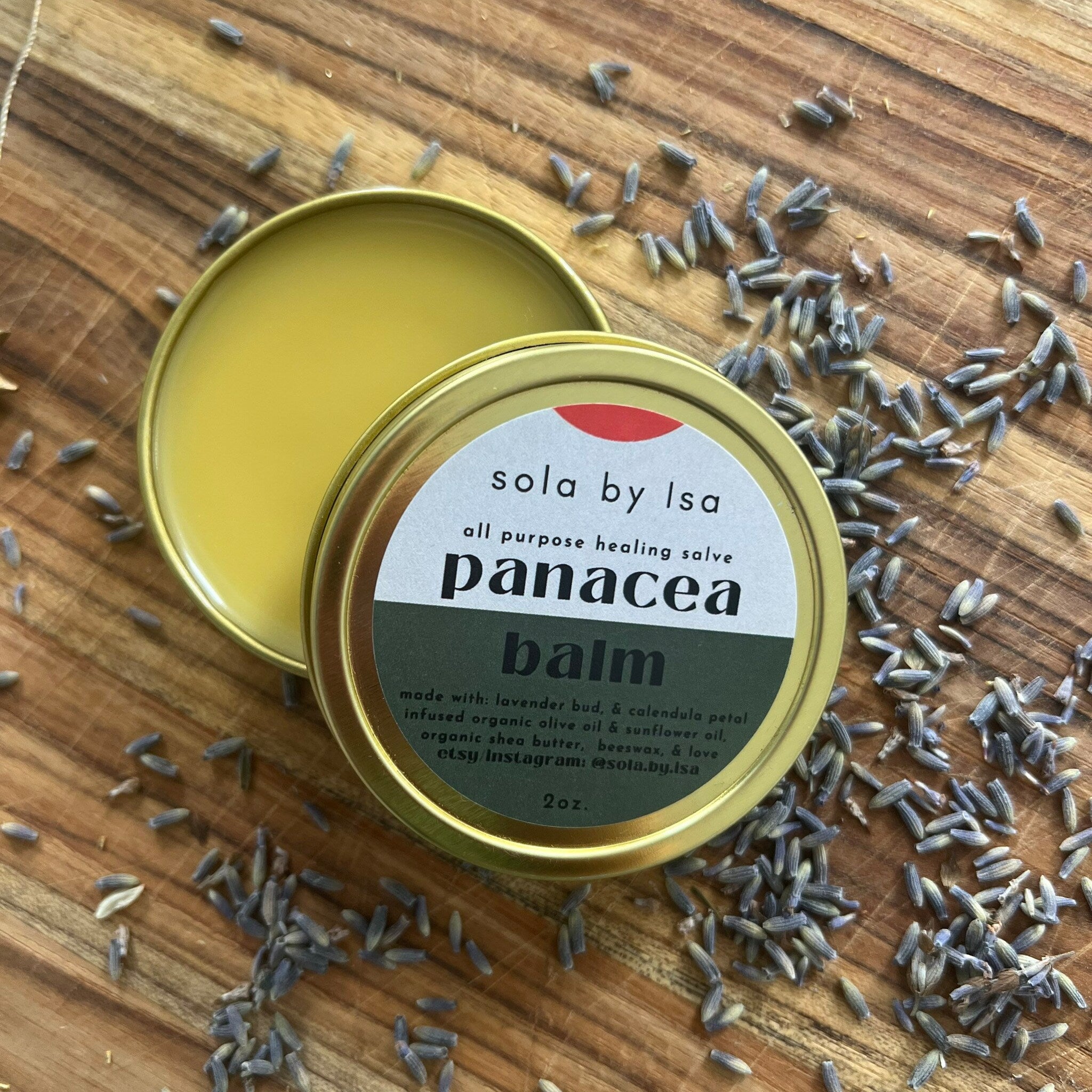 Body balm in open gold tin with yellow balm, sola by Isa label, and lavender buds scattered on wood