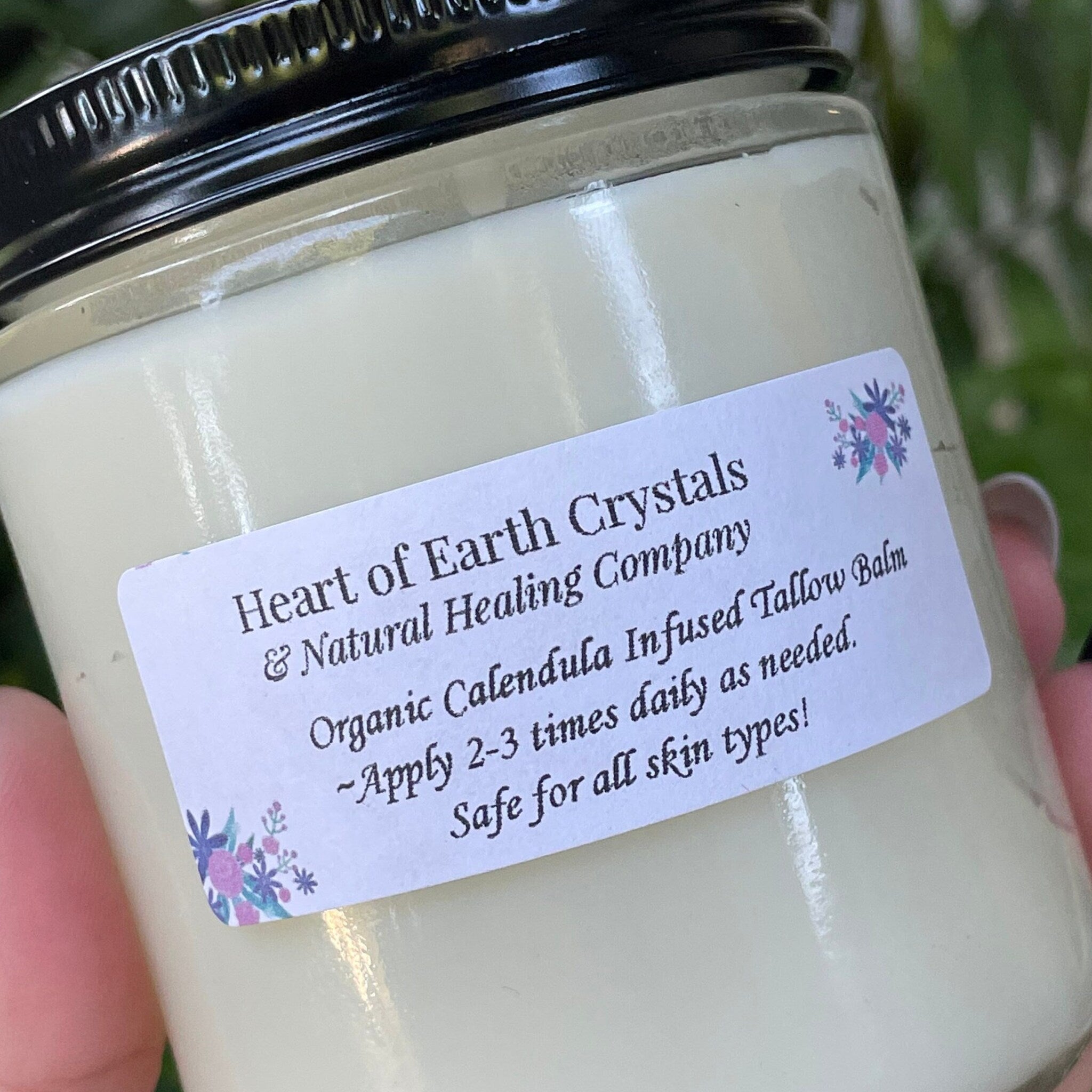Tallow balm jar with black lid, white label, and floral accents, Heart of Earth Crystals brand