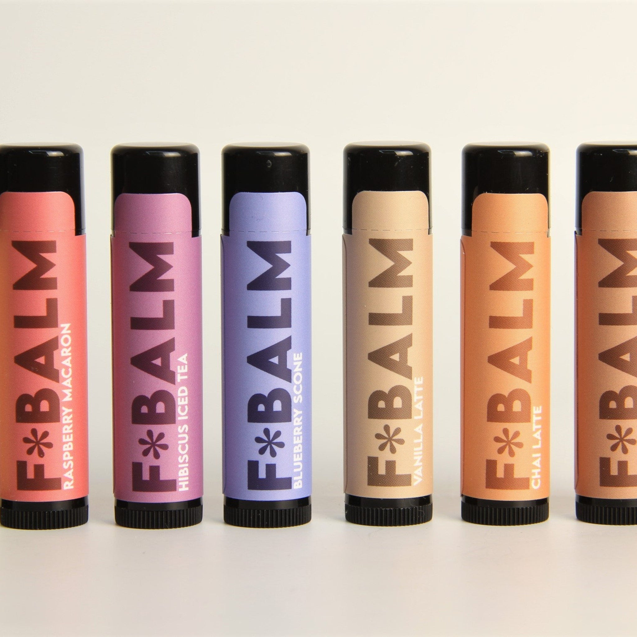 Lip balm tubes with various colors and F*BALM brand text, arranged in a row against a white background