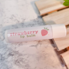 Strawberry lip balm tube with pink text, strawberry illustration, and white cap on marble surface
