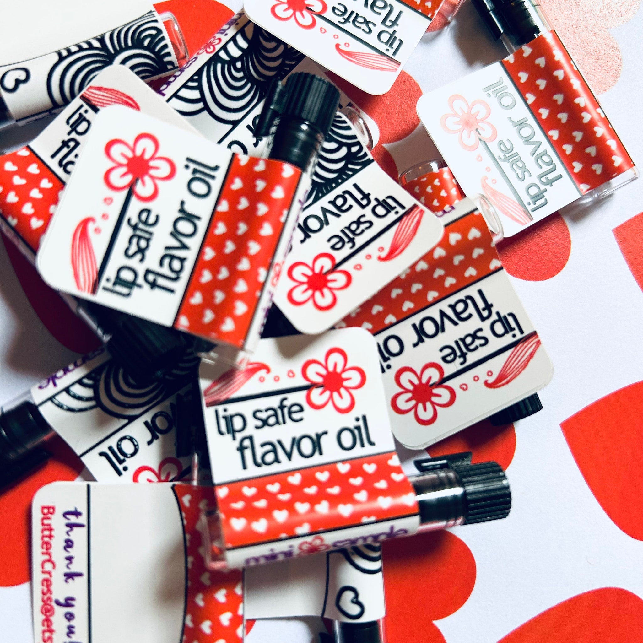 Lip safe flavor oil with red heart pattern and black and white label, ButterCress brand visible on some labels