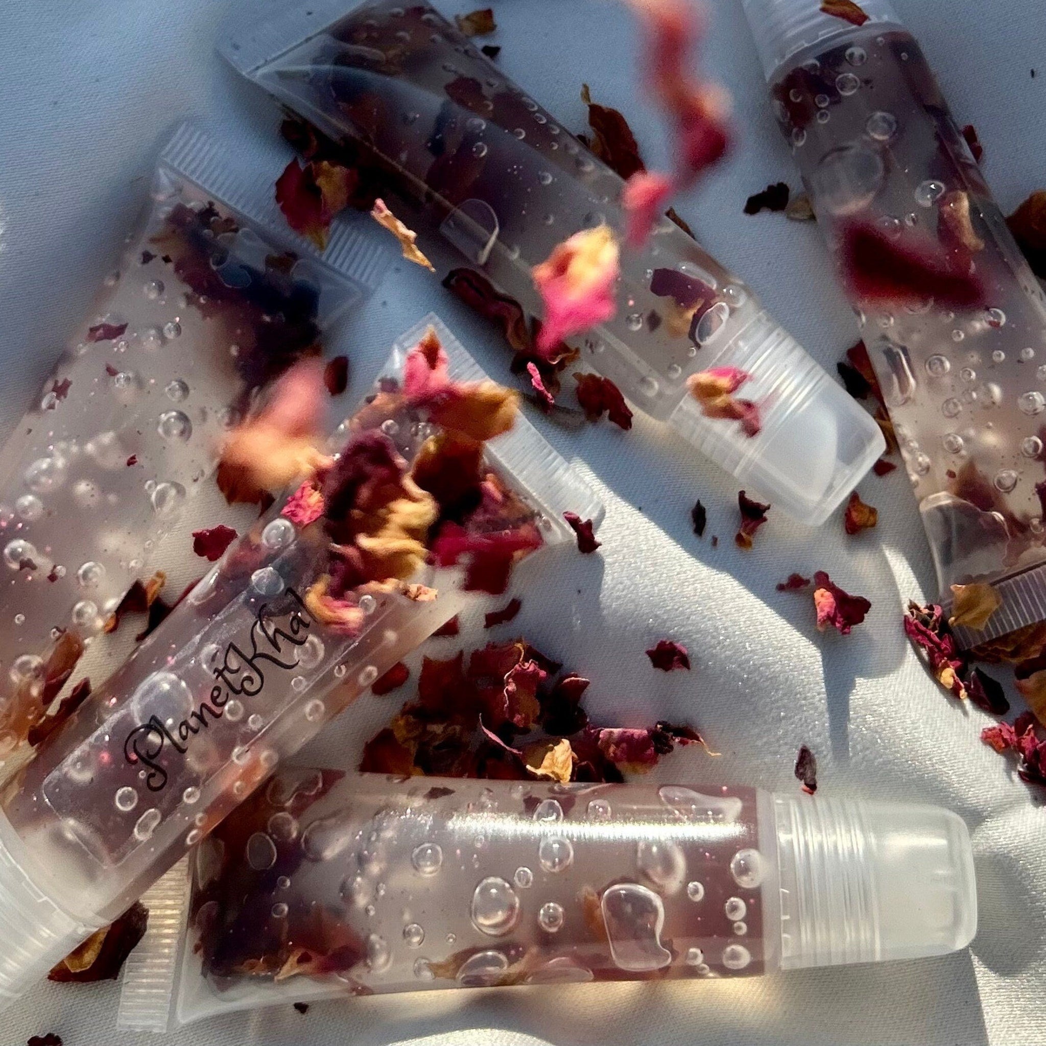 Lip gloss tubes with clear plastic, red rose petals, and "Planet Khal" text