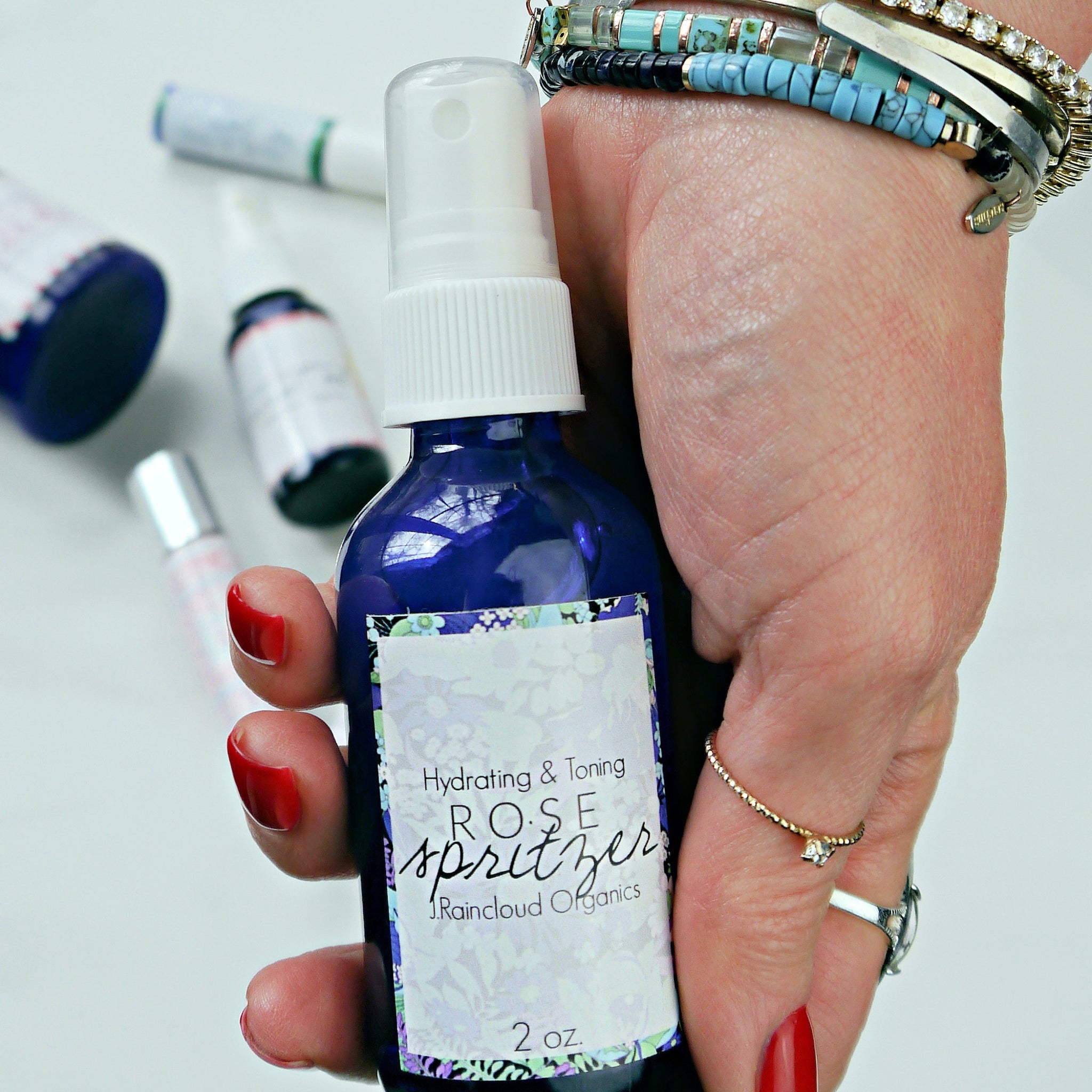 Rose spritzer bottle, blue glass, white label with floral border, held in hand with jewelry