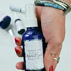 Rose spritzer bottle, blue glass, white label with floral border, held in hand with jewelry