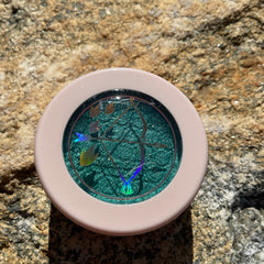 Close-up of emerald green shimmery eye shadow with golden flecks in round compact