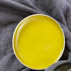 Yellow balm in a silver tin, on dark blue fabric background