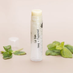 Lip balm tube with white and clear plastic, pale yellow balm, and green leaves around it