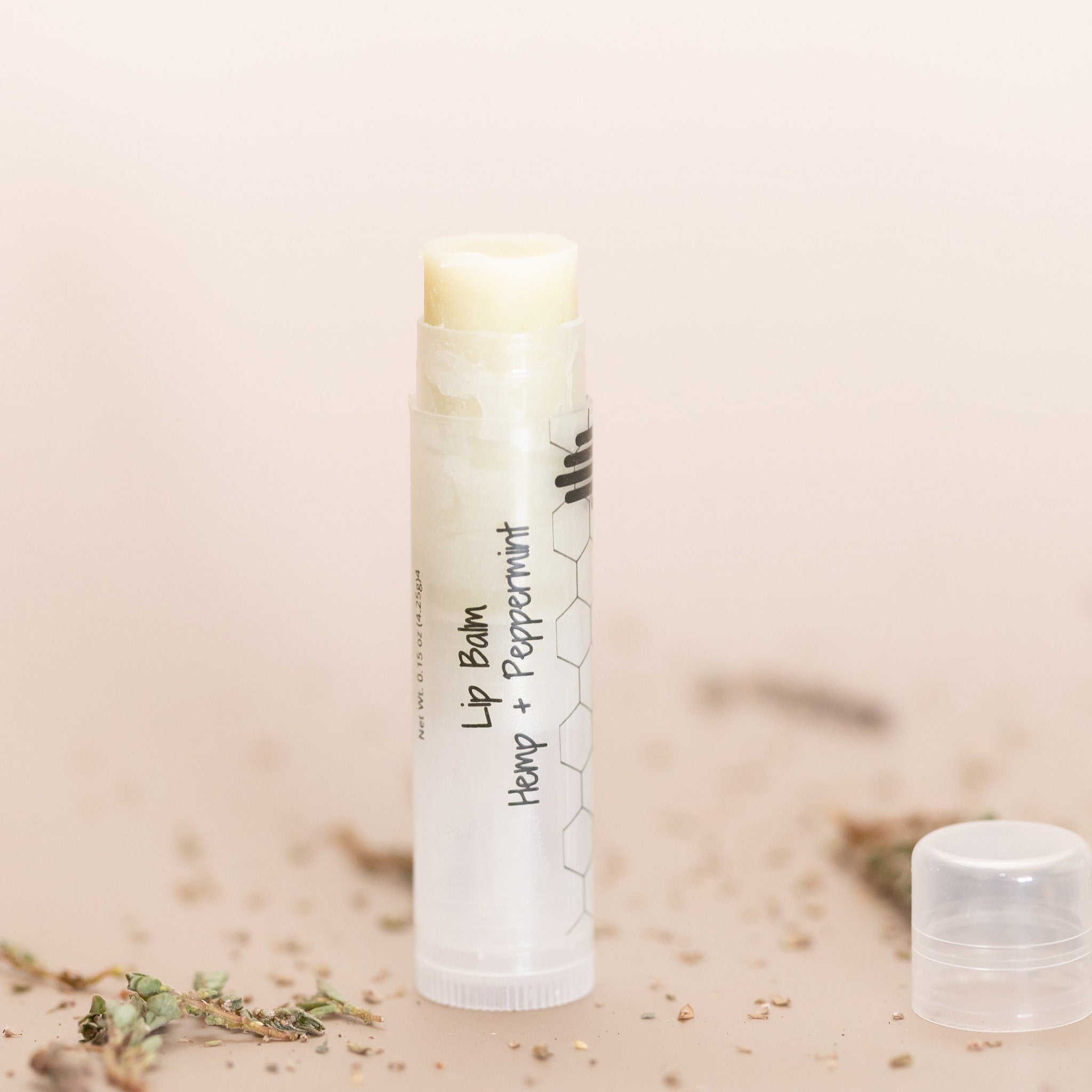 Lip balm stick with white and clear tube, Hemp + Peppermint text visible, with lid off