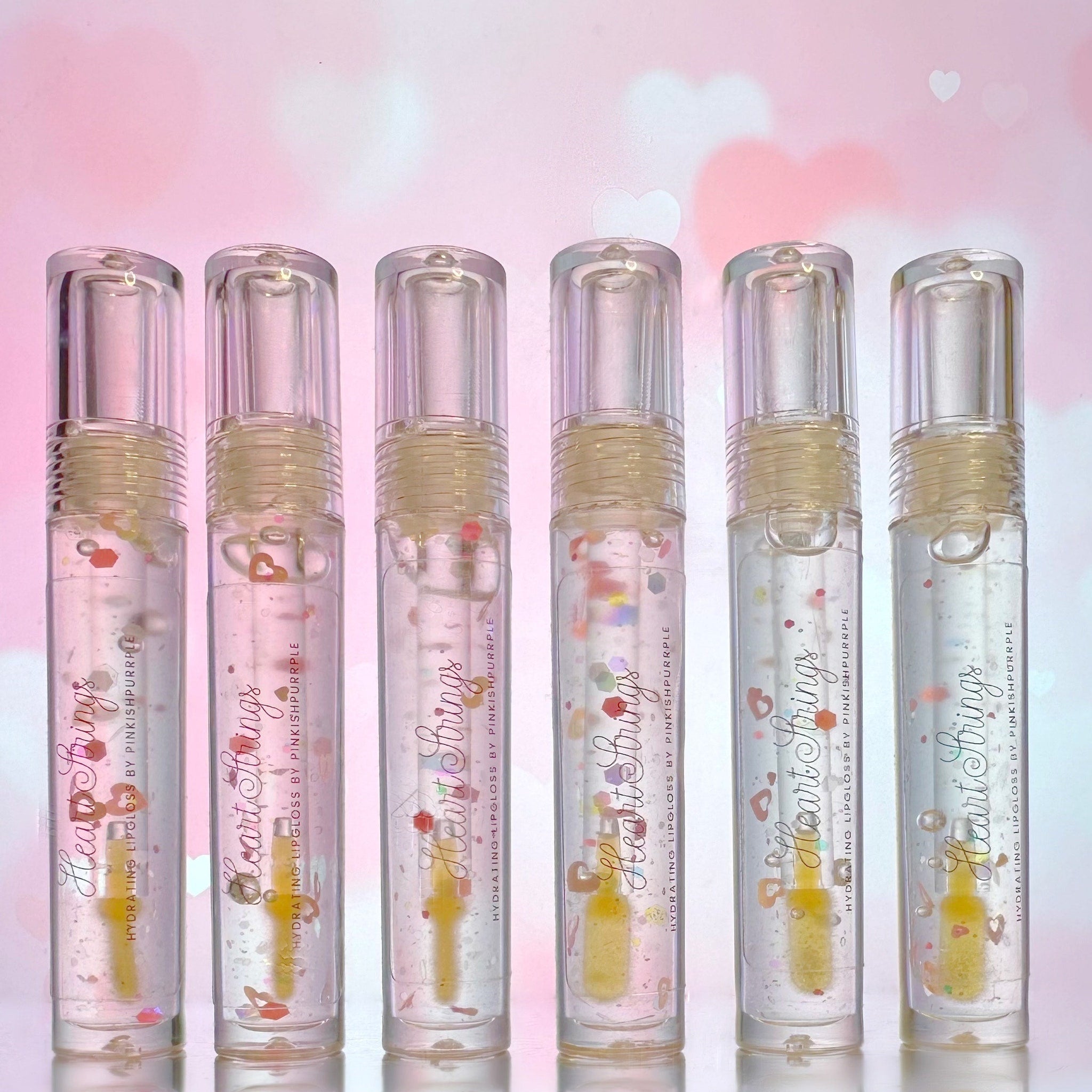 Lip gloss tubes with clear plastic, silver caps, and Heart Strings text, with glitter inside
