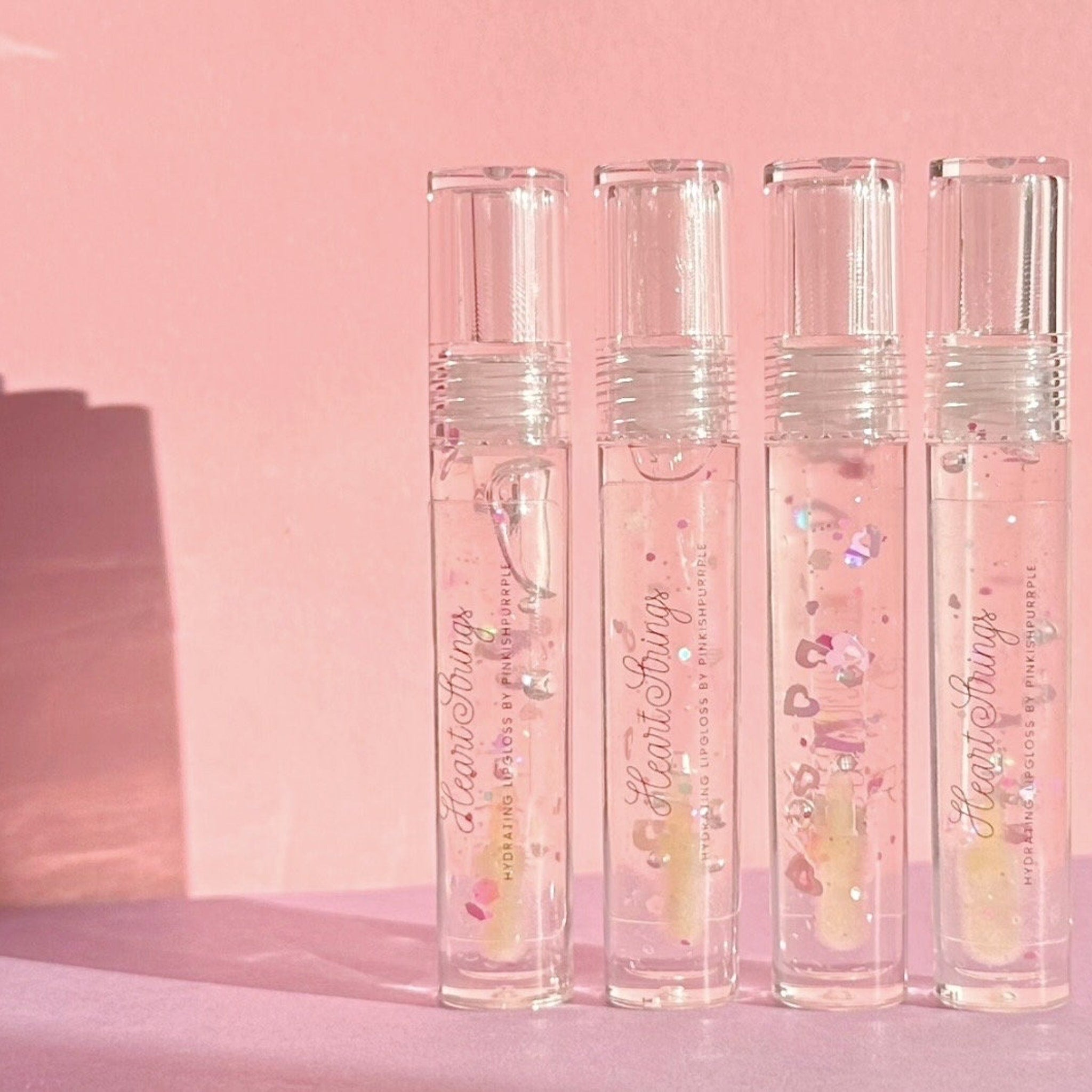 Lip gloss tubes with clear, glass-like material, pink glitter, and Heart Strings label