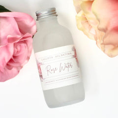 Rose water bottle, frosted glass, silver cap, Callista Naturals label, pink roses in background