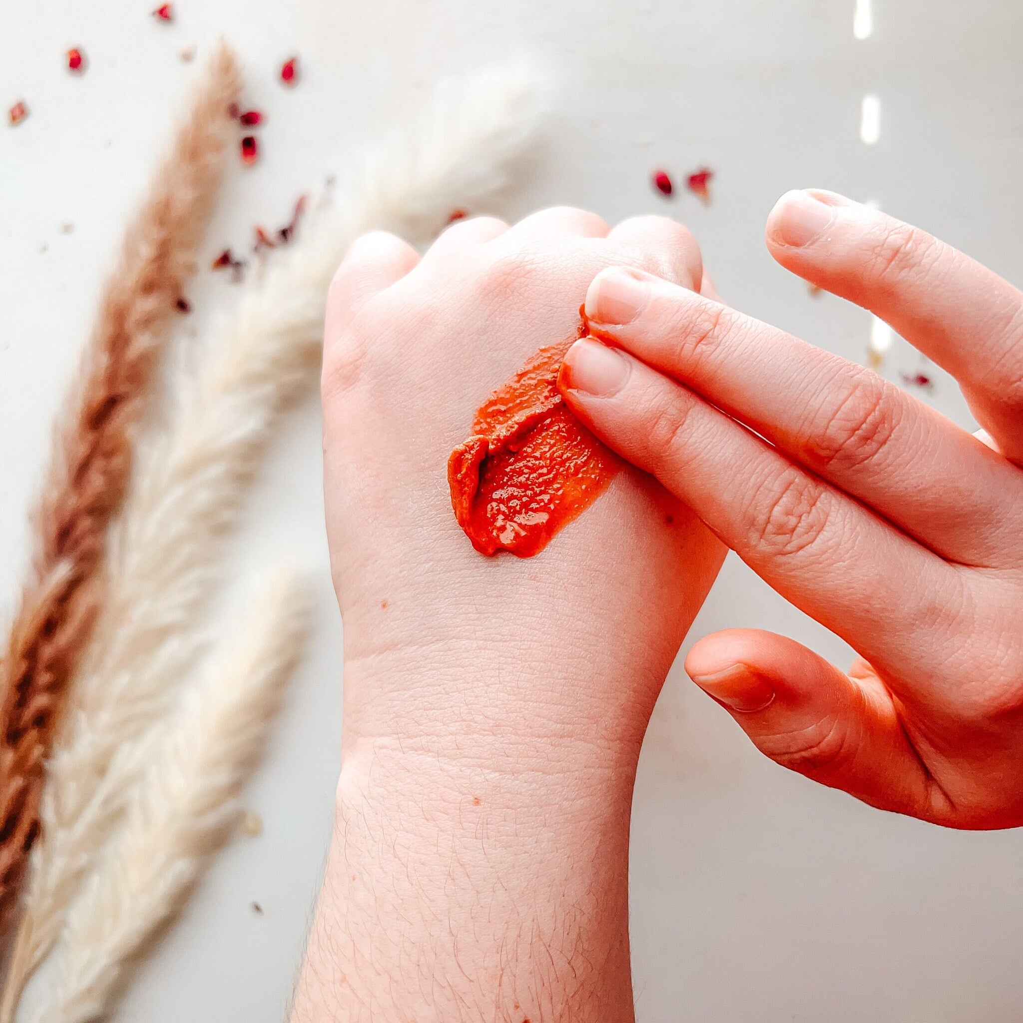 Red cream applied to hand, visible texture, white background with floral accents