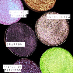 Close-up of fingertips applying shimmering trichrome eyeshadow with color-shifting glitter to eyelid