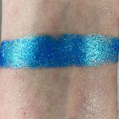 Close-up of a hand applying shimmering bronze eye shadow from the Charm palette with a fluffy brush
