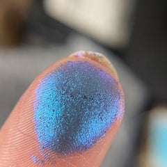 Close-up of hand applying shimmery taupe eyeshadow from palette with a fluffy blending brush