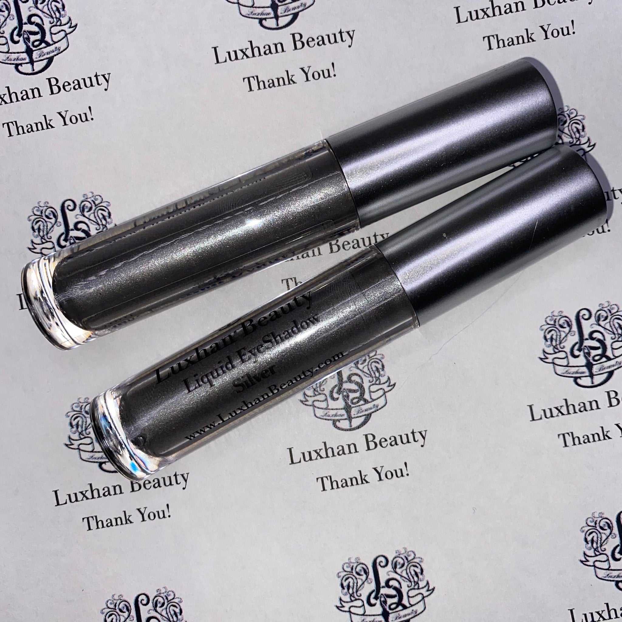 Silver glitter liquid eyeshadow bottle with sleek metallic cap, displayed upright on marble surface