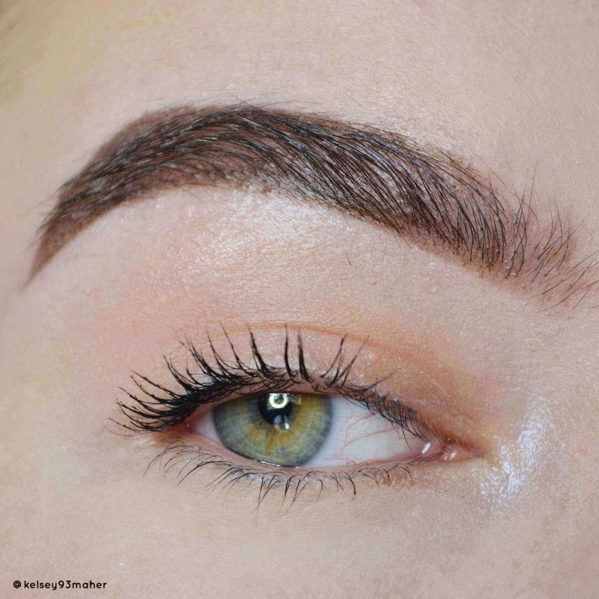 Eye close-up with green iris, dark eyelashes, and brown eyebrow on fair skin