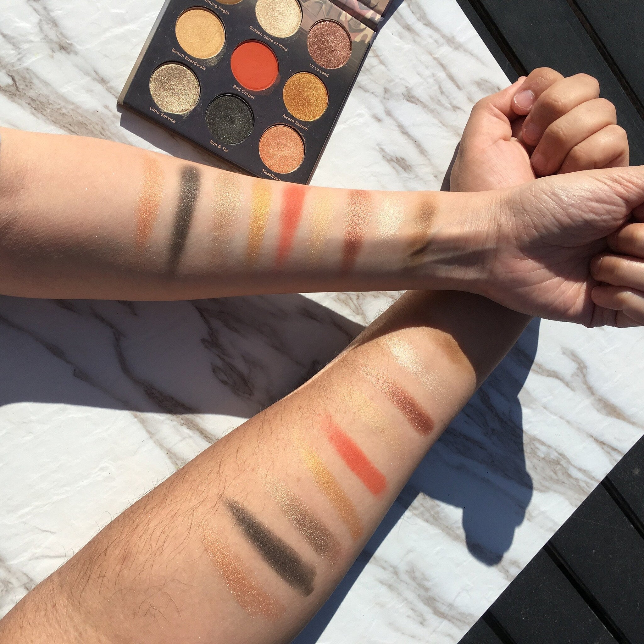 Eyeshadow palette with gold, orange, and black shades swatched on arms for color comparison