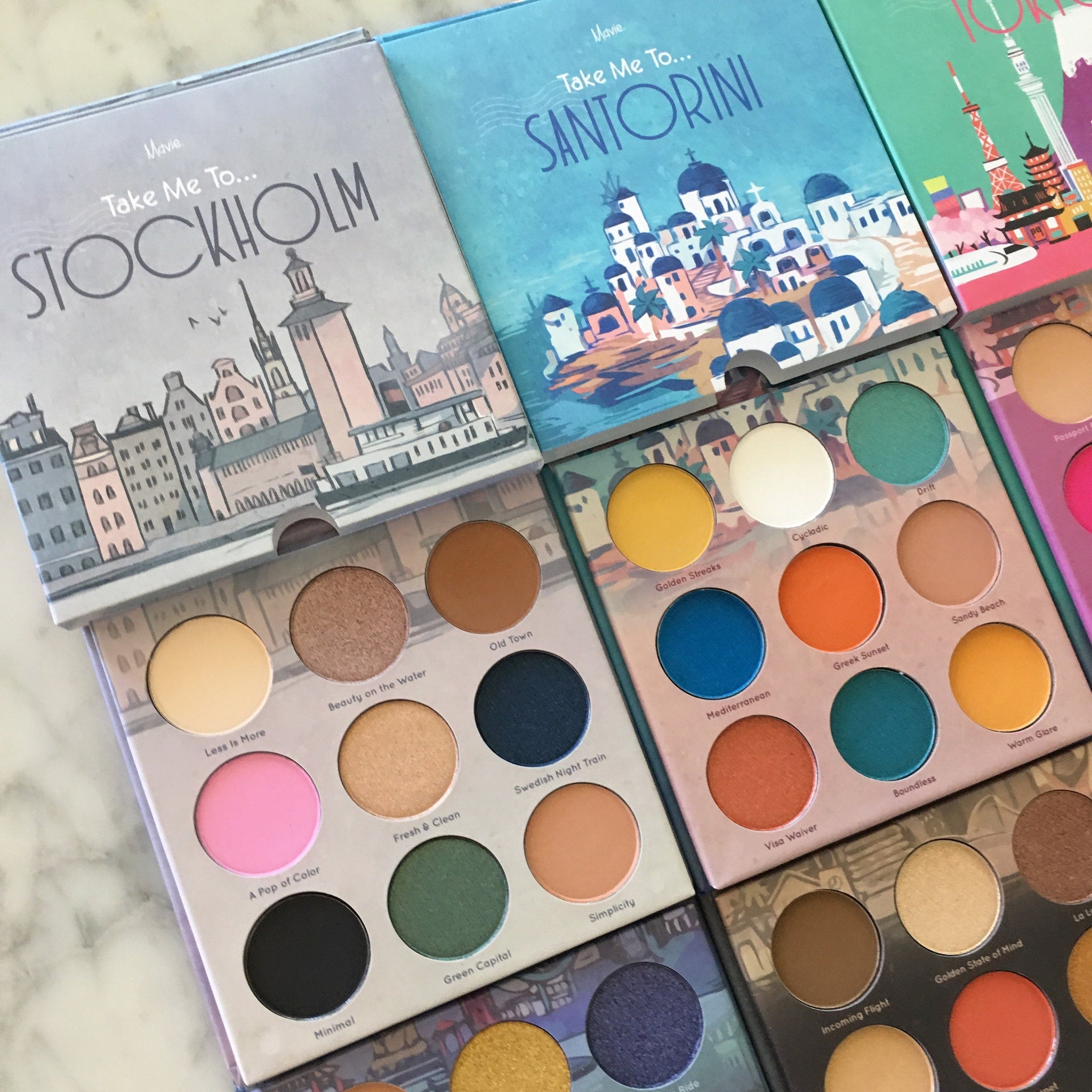Eyeshadow palettes with Mavie Take Me To branding, colorful eyeshadows, and city illustrations on the packaging