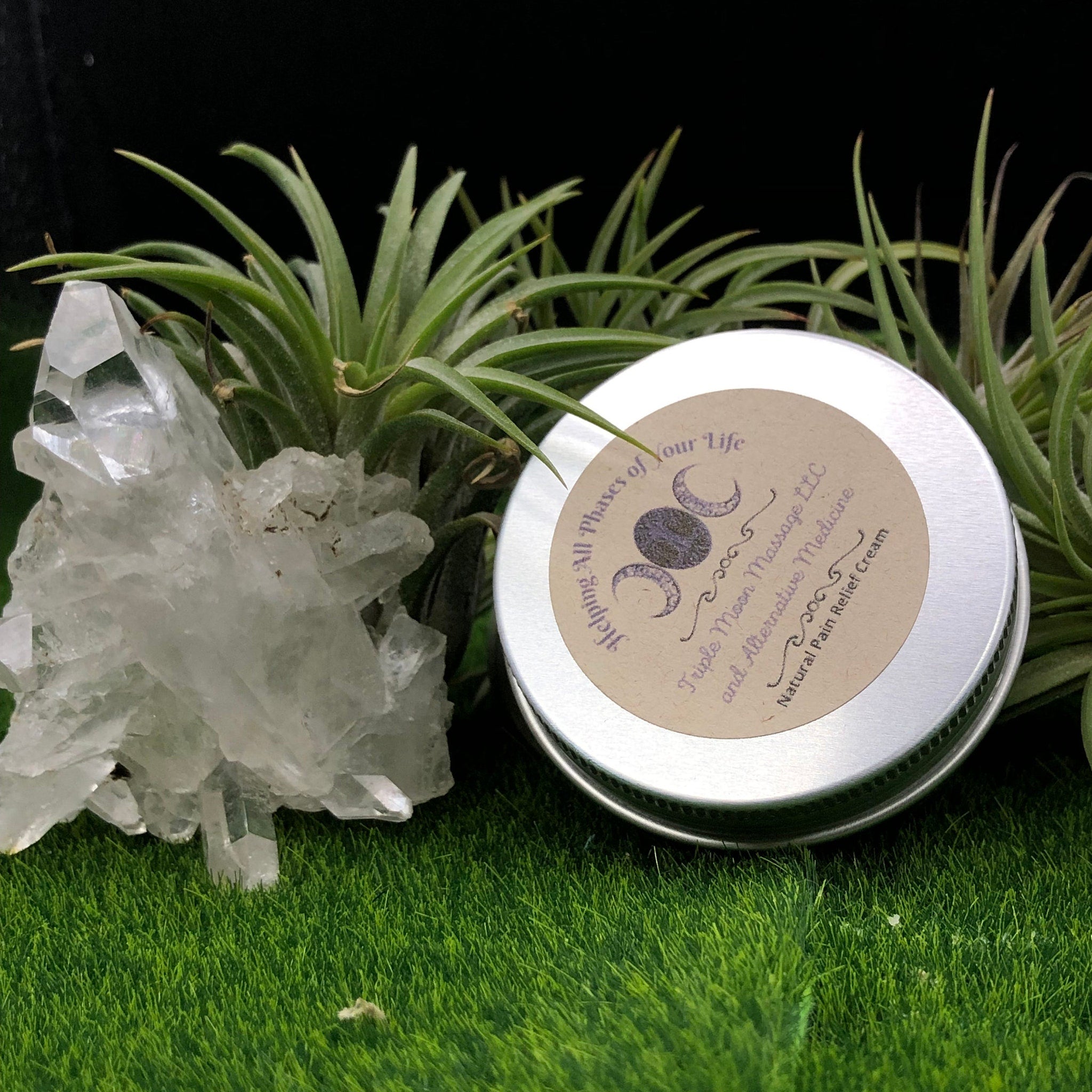 Pain relief cream in silver tin with brand label, clear crystal, and green grass background