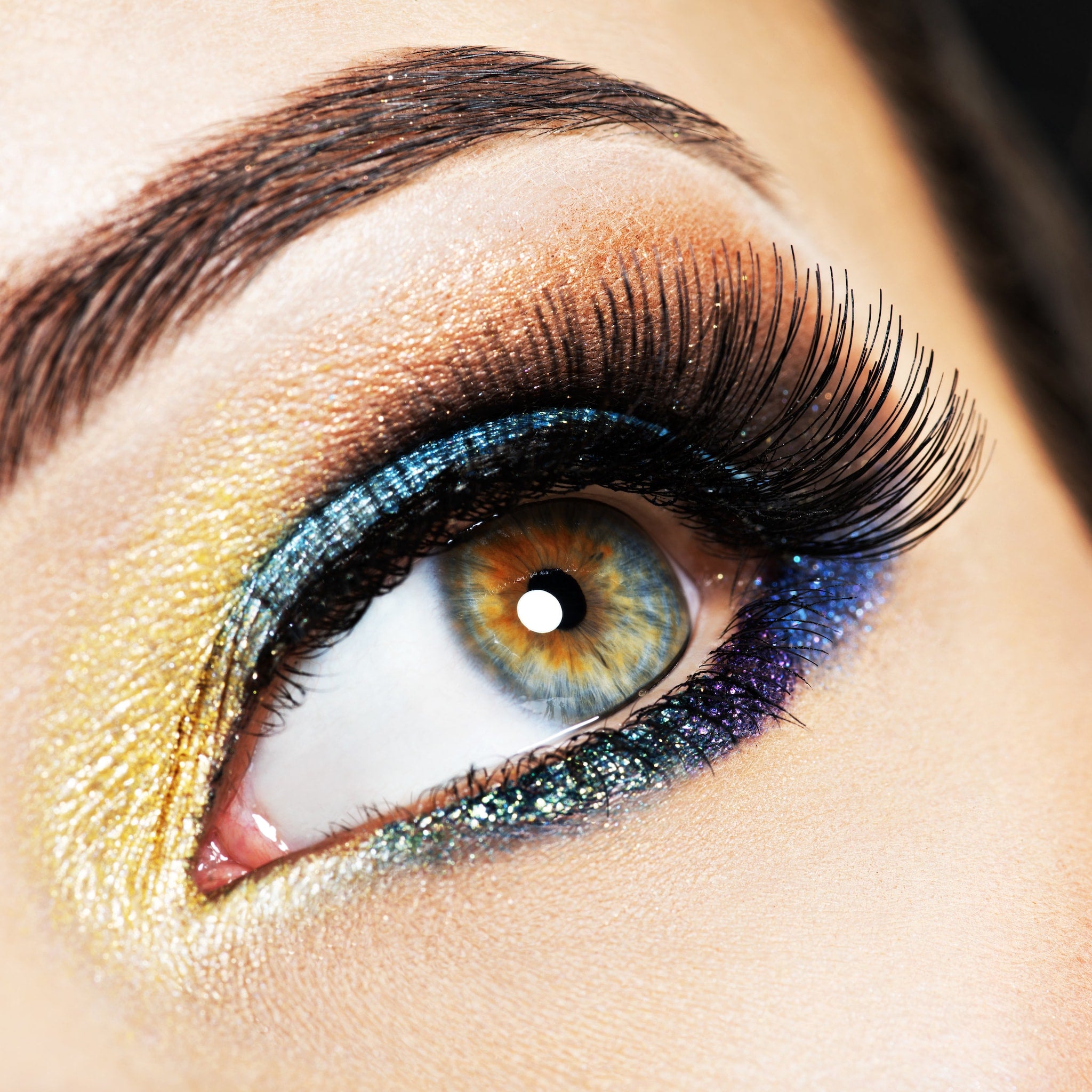 Eye makeup with gold, blue, and black glitter applied, close-up of eye with long lashes
