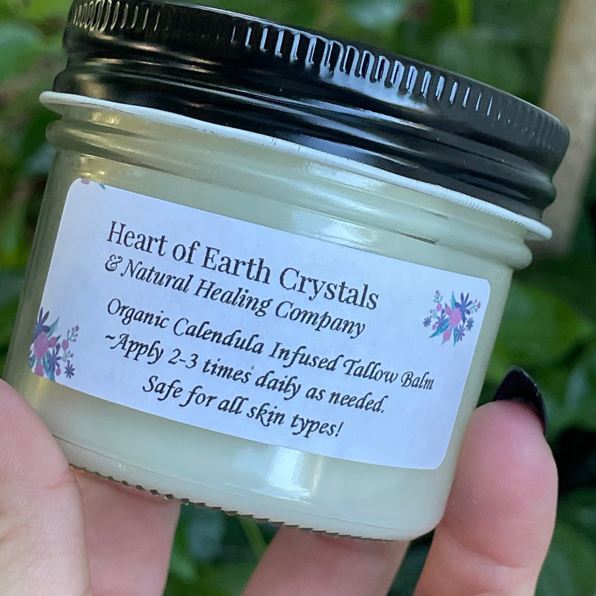 Tallow balm jar, green glass, black lid, Heart of Earth Crystals label, held in hand