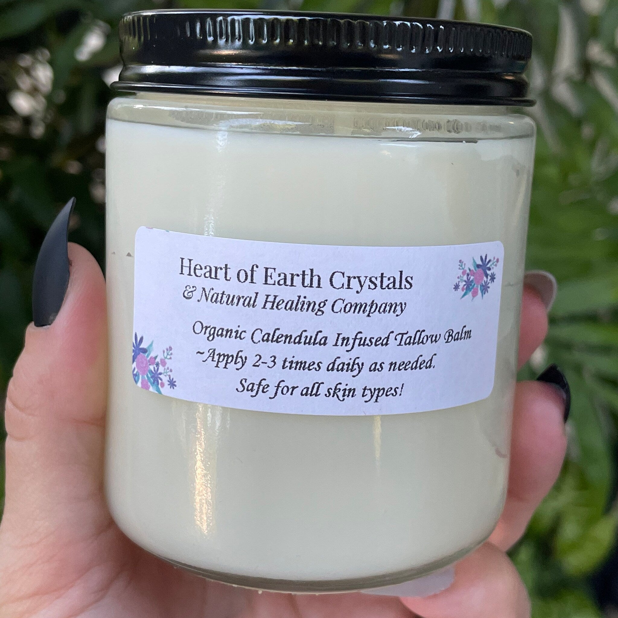 Tallow balm in glass jar with black lid, held in hand, Heart of Earth Crystals label