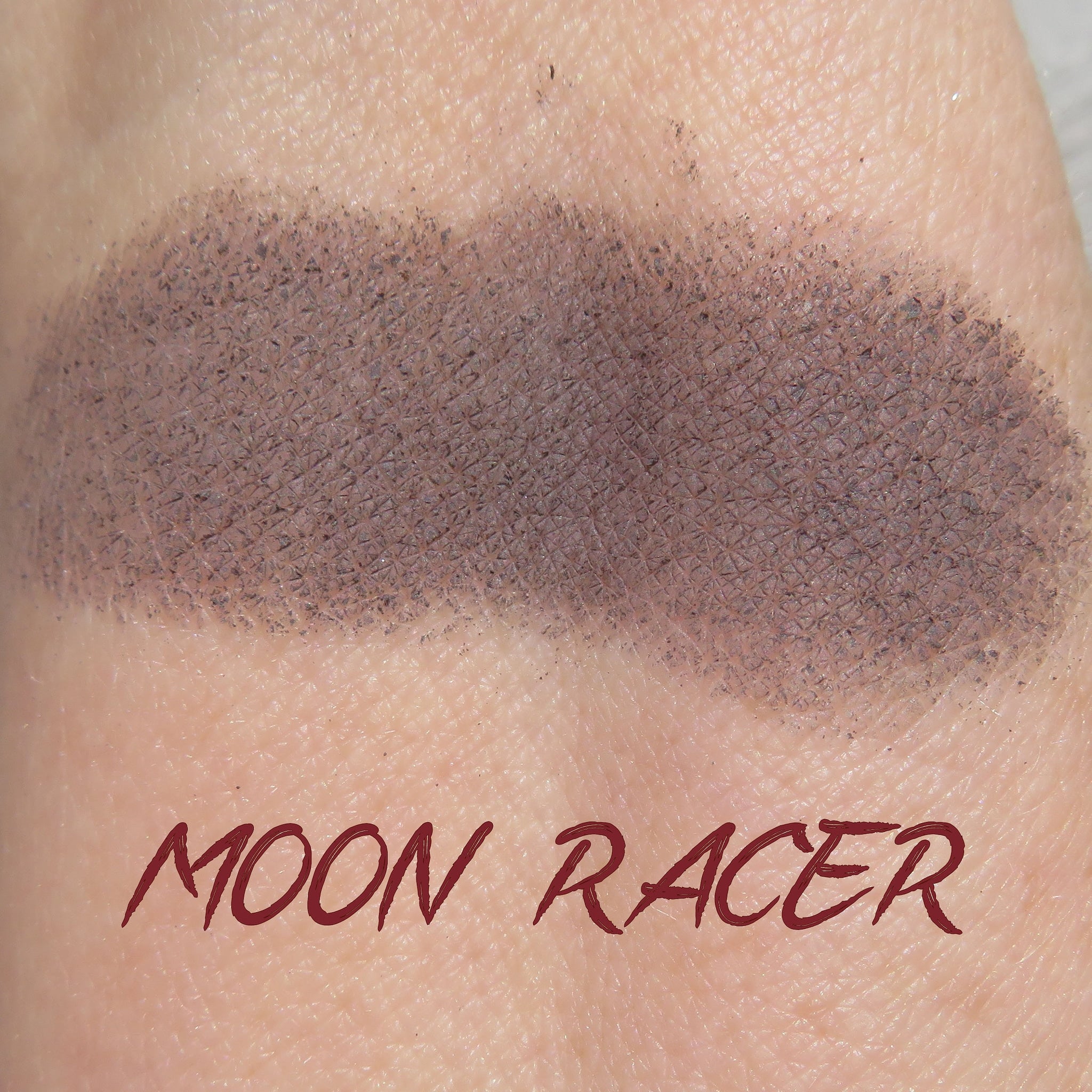 Eyeshadow swatch, gray-brown color with textured appearance, on skin, Moon Racer text visible