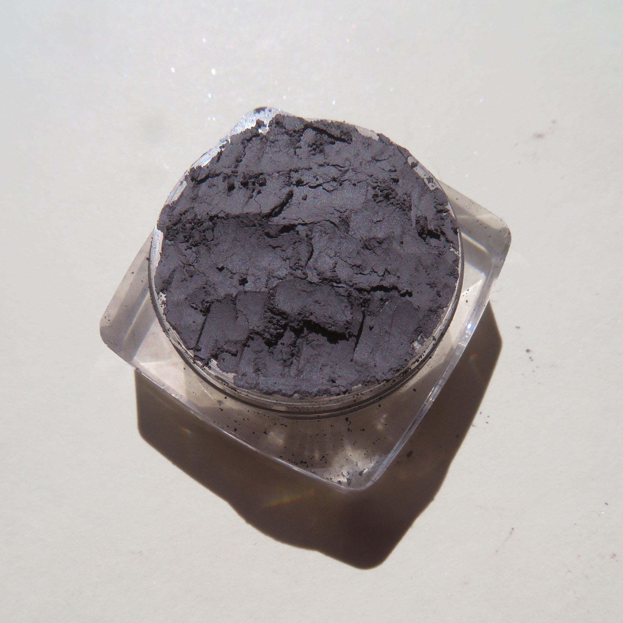 Dark gray powder in clear plastic container, textured surface, angled view