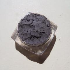 Dark gray powder in clear plastic container, textured surface, angled view