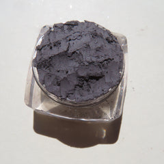 Eyeshadow in dark gray powder with textured appearance in clear plastic container
