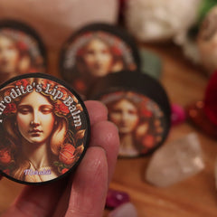 Lip balm tin with woman illustration, text, and black rim, held in hand