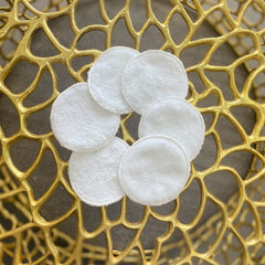 Makeup remover pads, white cotton rounds, arranged in a flower shape on gold surface