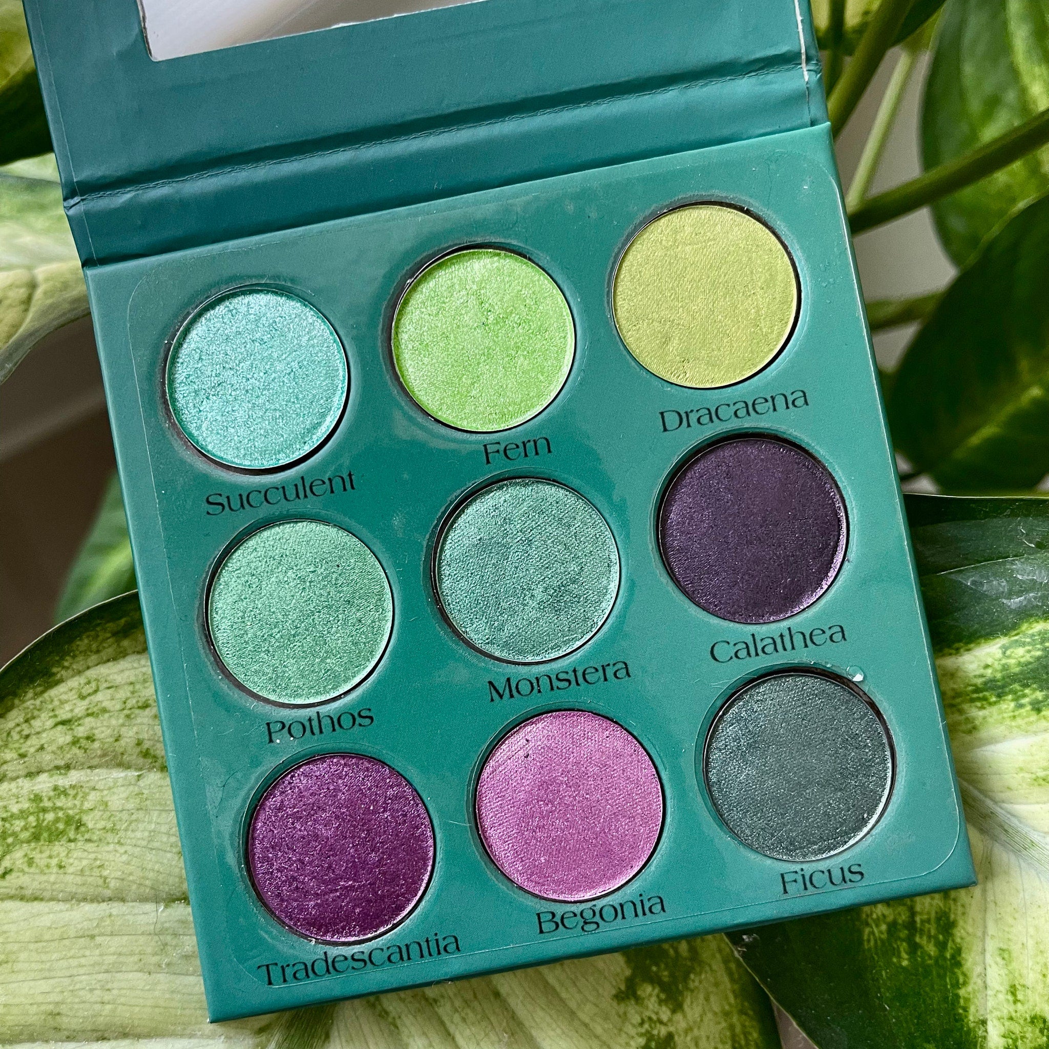 Close-up of botanical-inspired eyeshadow palette showing matte green and shimmer gold pans with floral imprint details