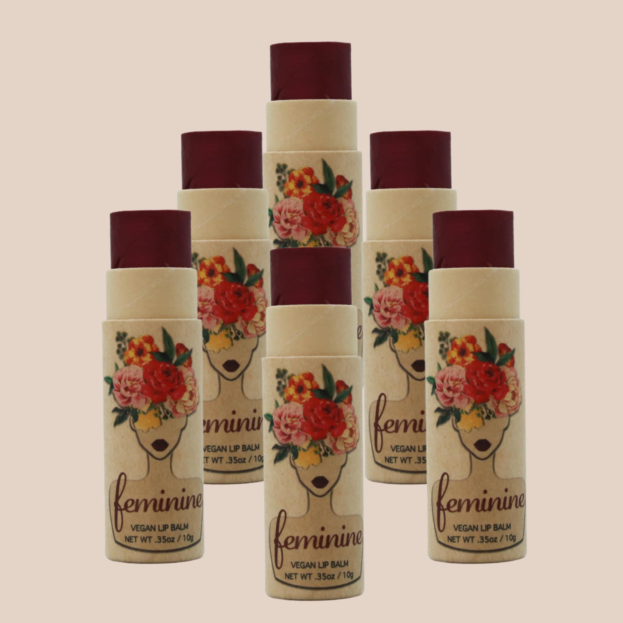 Lip balm tubes with burgundy tops, floral print, and "feminine" text on natural paper