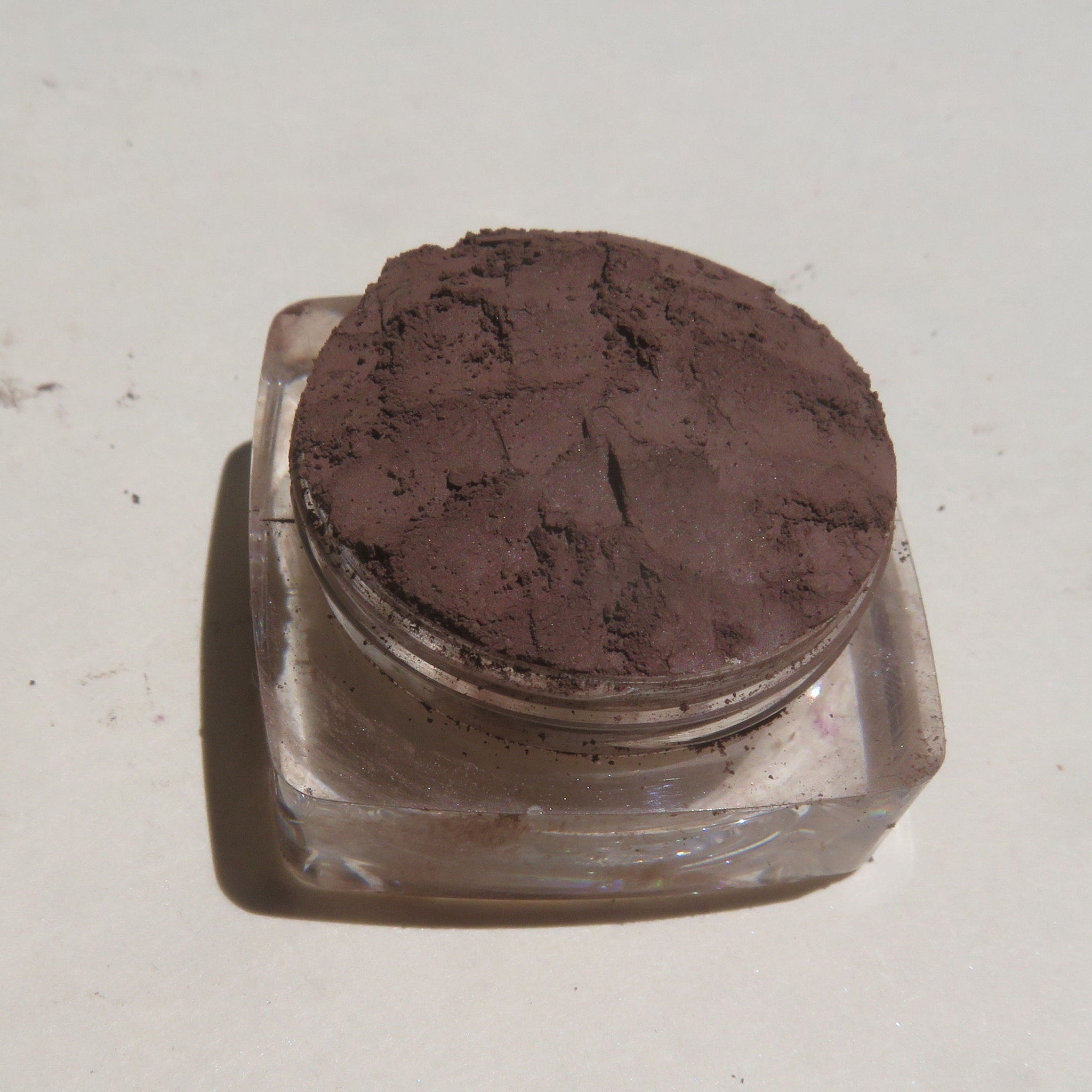 Hand applying dark brown matte mineral eye shadow with a fluffy brush for a soft, blended look on the eyelid