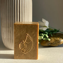 Soap bar with brown color, carved design, and rectangular shape, displayed with a vase and stone