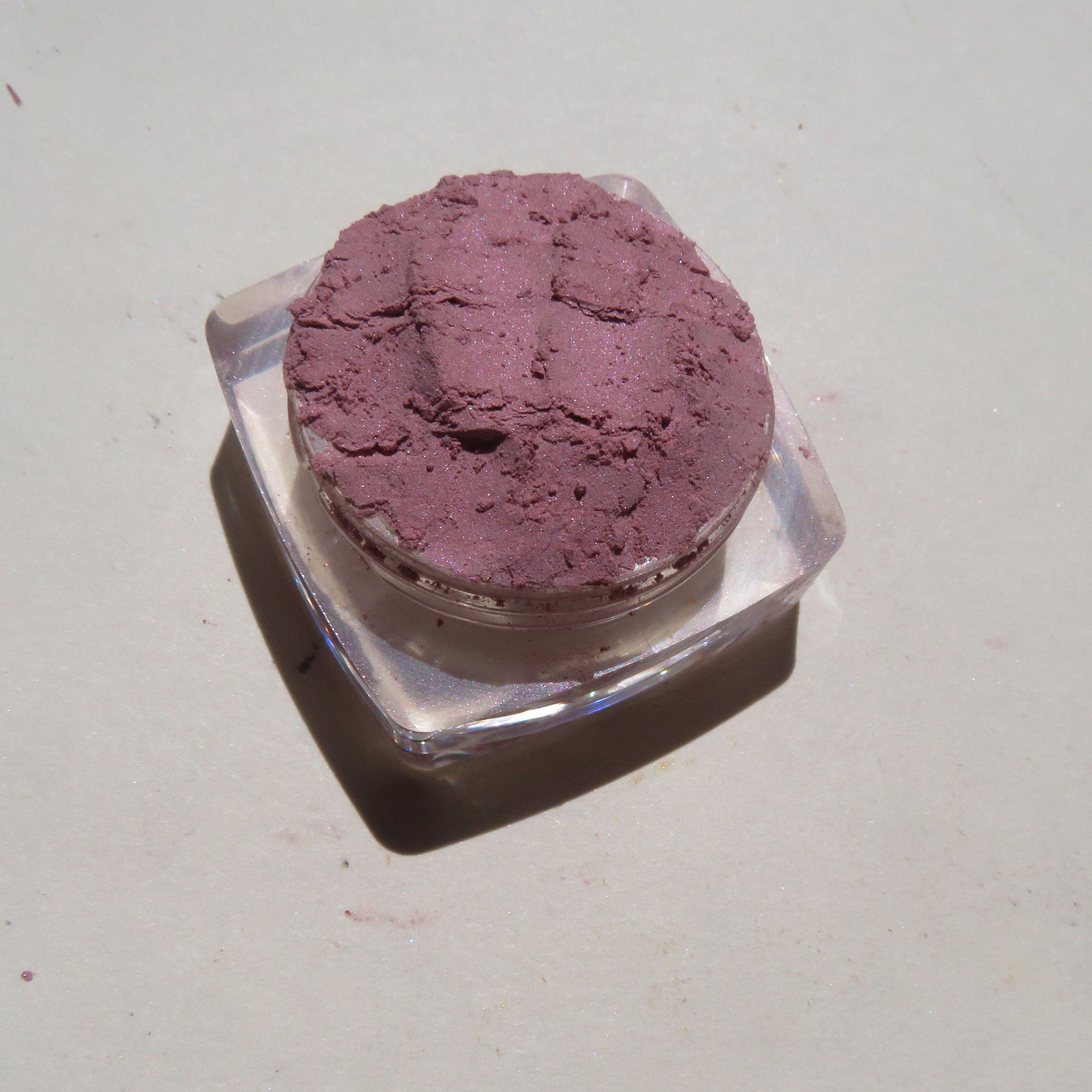 Close-up of loose pale mauve mineral eyeshadow powder with soft shimmer in a small jar
