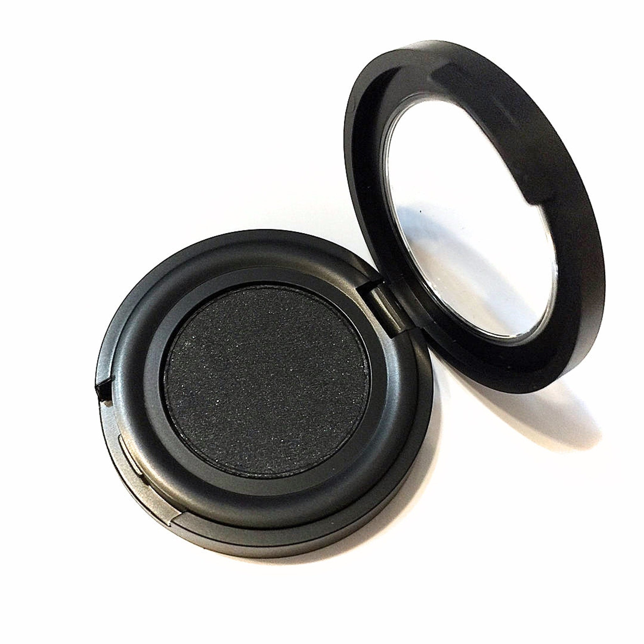 Side view of black pressed mineral eyeshadow in compact showing smooth matte texture and square pan shape