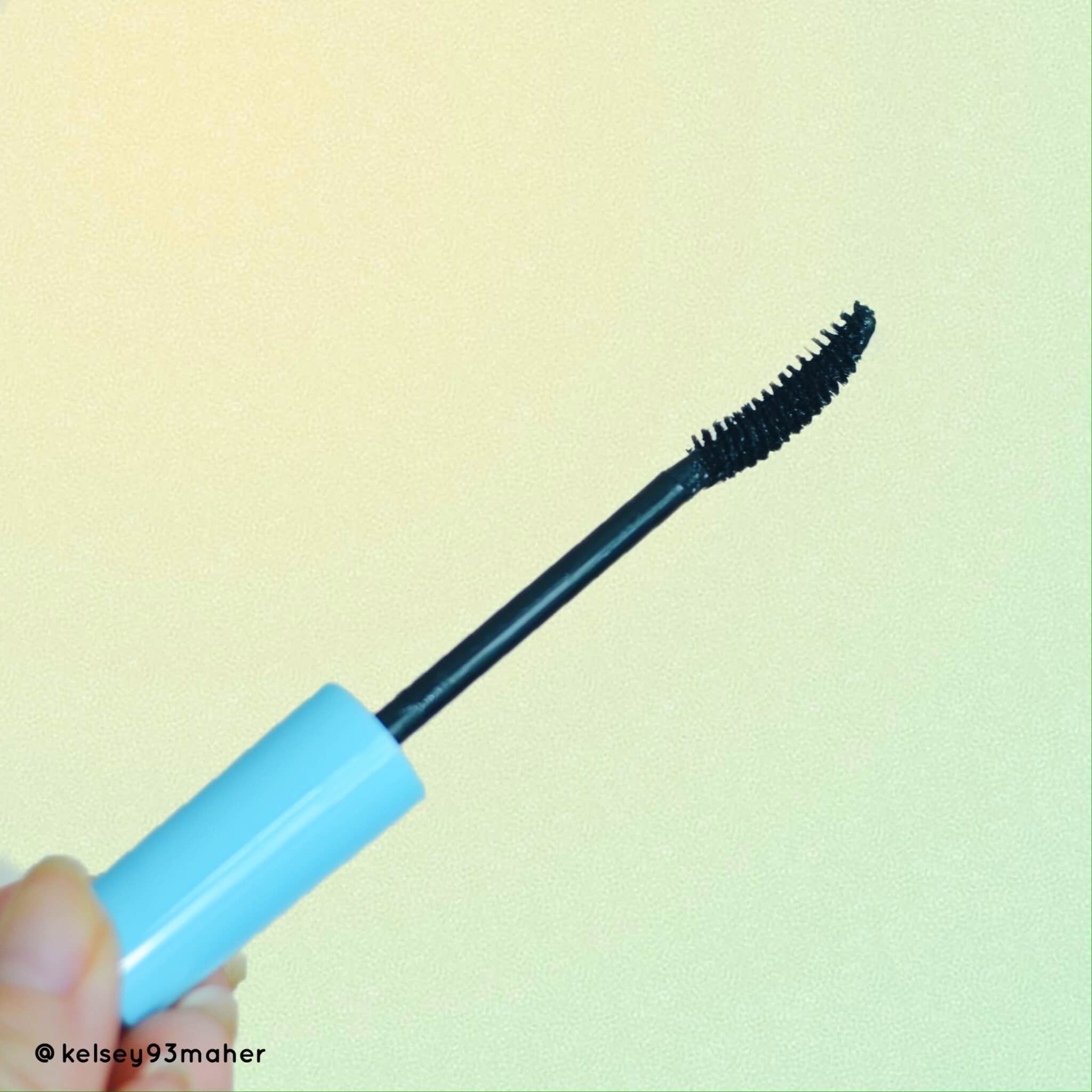 Mascara wand with black bristles, blue handle, and black applicator tip in hand