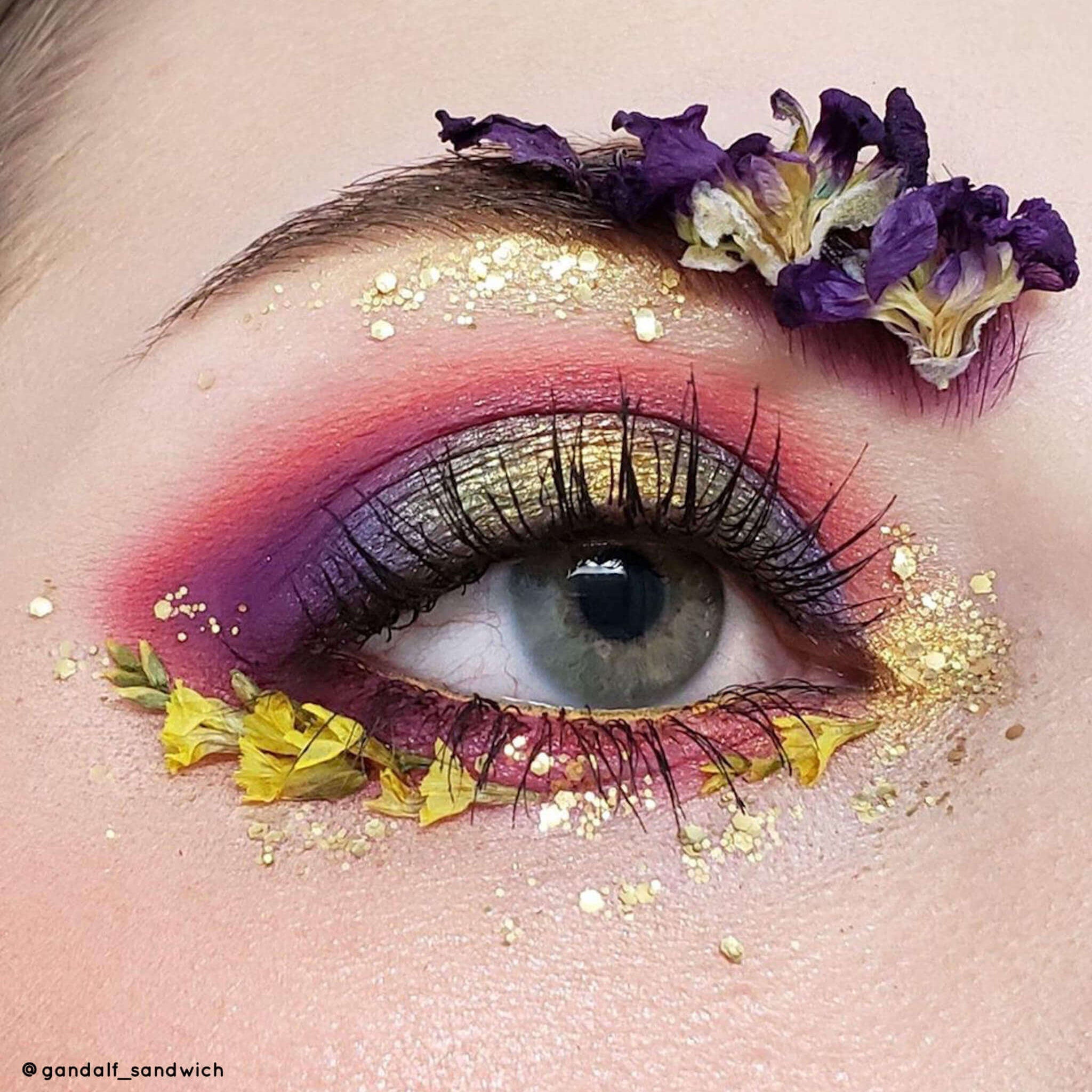 Eye makeup with purple, gold, and red eyeshadow, decorated with flowers and glitter, close-up view