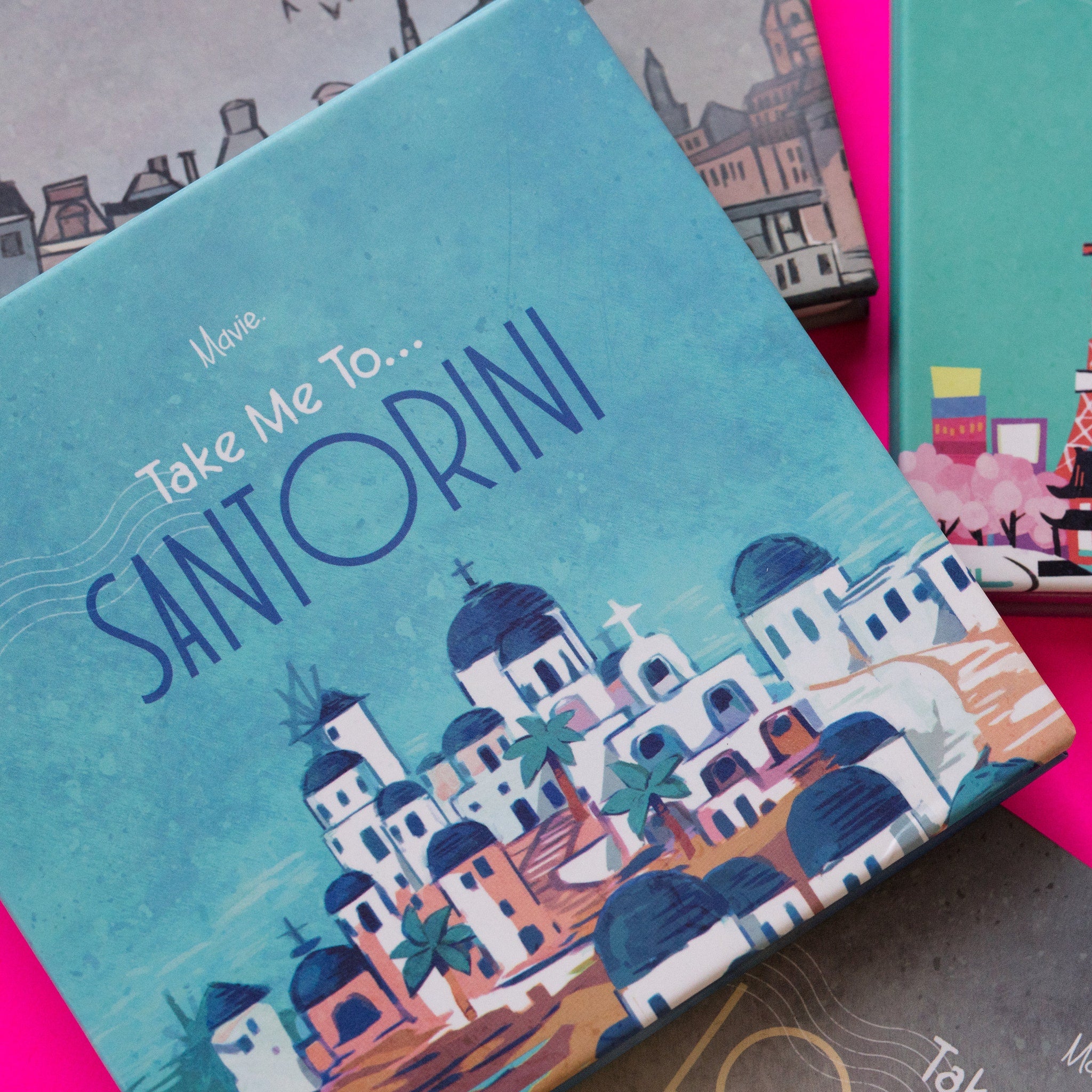 Travel-themed box with blue and white illustration, Mavie Cosmetics branding, and Take Me To Santorini text