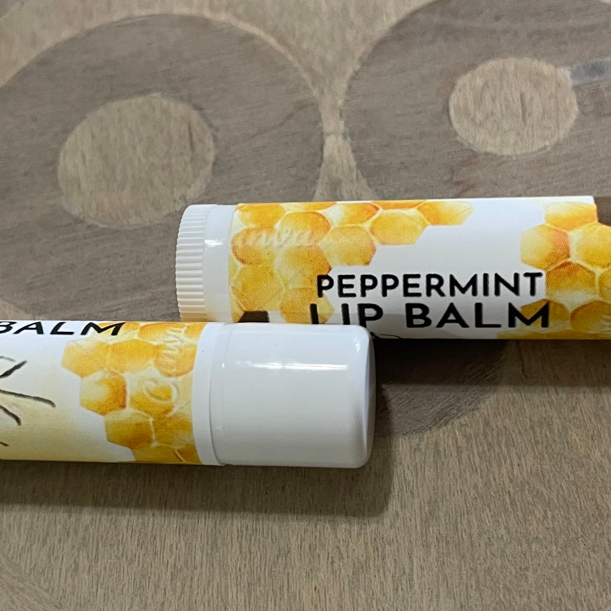 Peppermint lip balm tubes with white and yellow honeycomb pattern, on wooden surface.