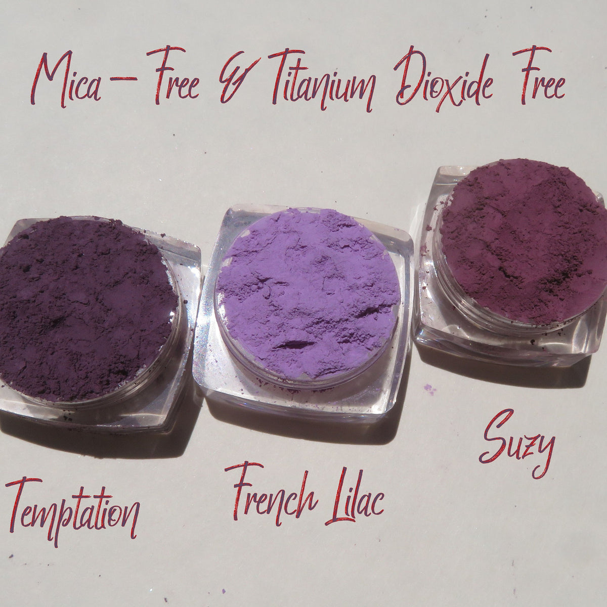 Matte purple mineral eyeshadow set in round jars with black lids, vegan loose powder displayed on white background