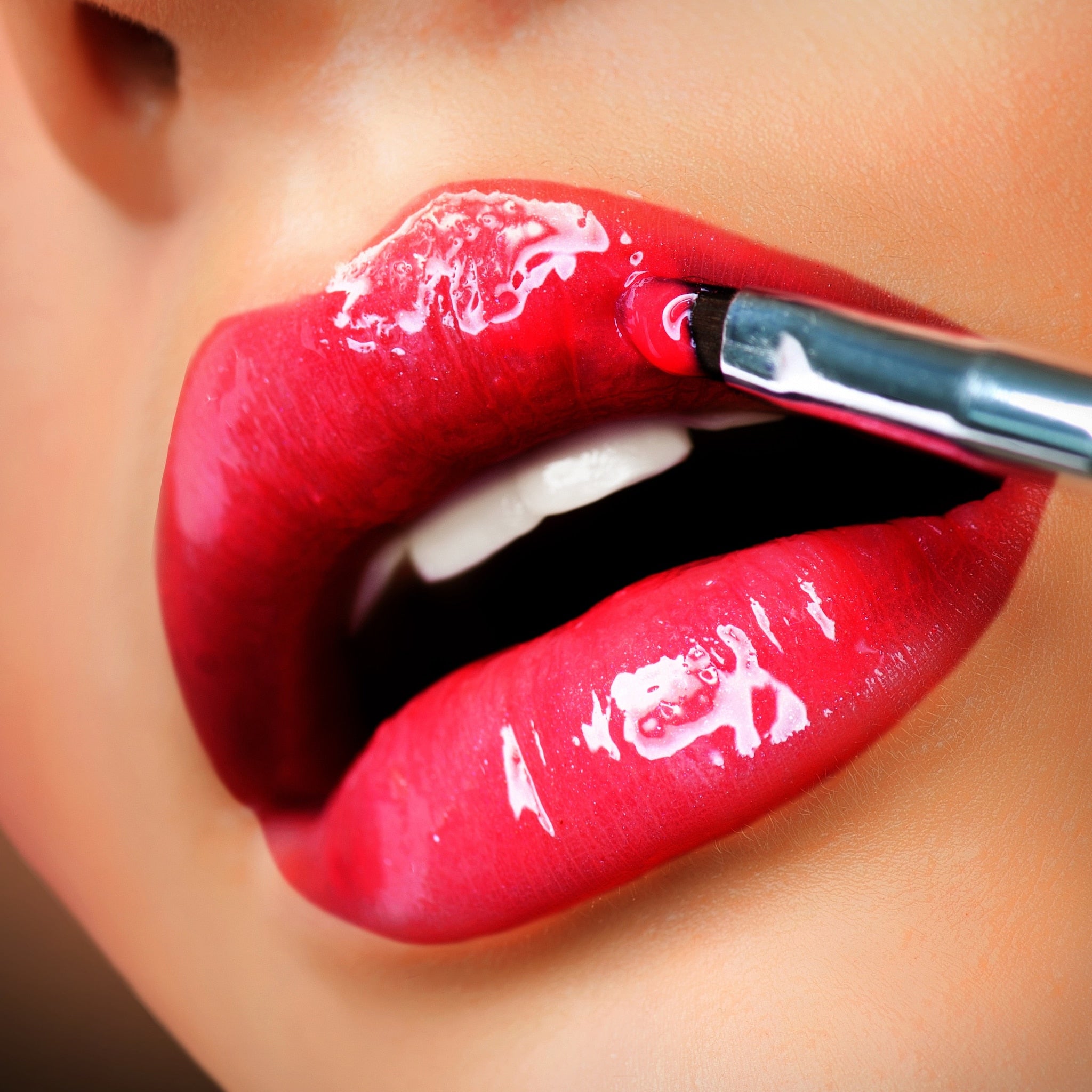 Red glossy lipstick being applied with a brush to the lips