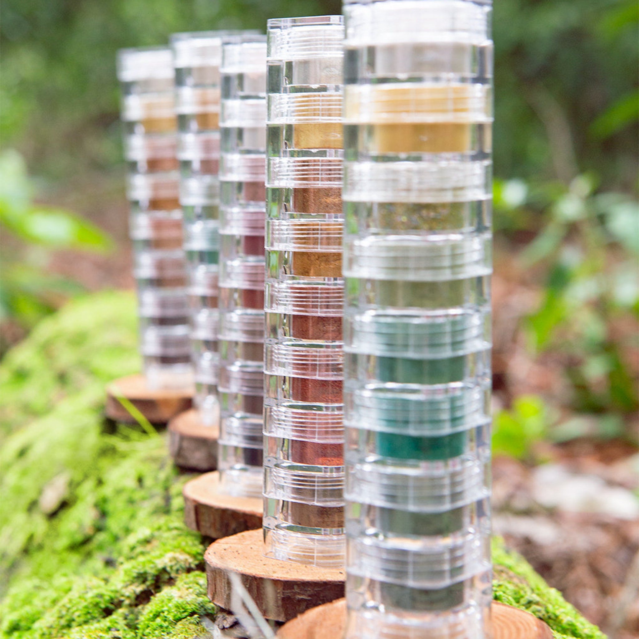 Clear plastic containers with colorful contents, arranged on wooden rounds, outdoors