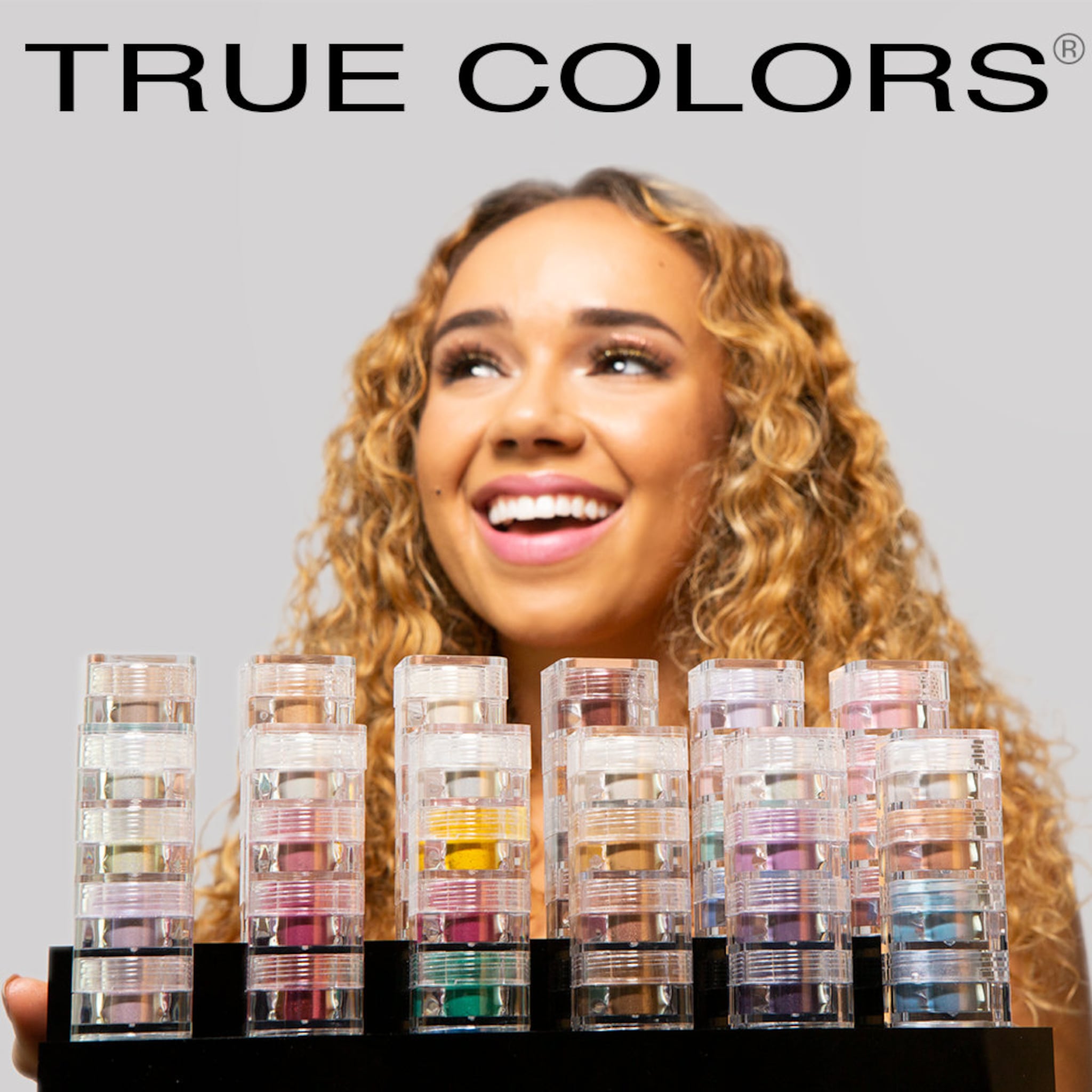 Makeup product display with clear plastic containers and colorful eyeshadows, TRUE COLORS brand name above
